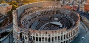 Veduta aerea panoramica del Colosseo a Roma durante il tramonto con i fori imperiali sullo sfondo.